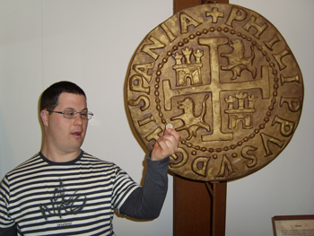 Un joven nos muestra una moneda actual comparándola con una replica de las de la época de los piratas.