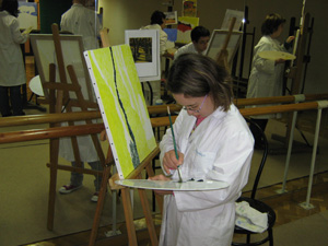 Una participantes toma pintura de la paleta para pintar el lienzo.